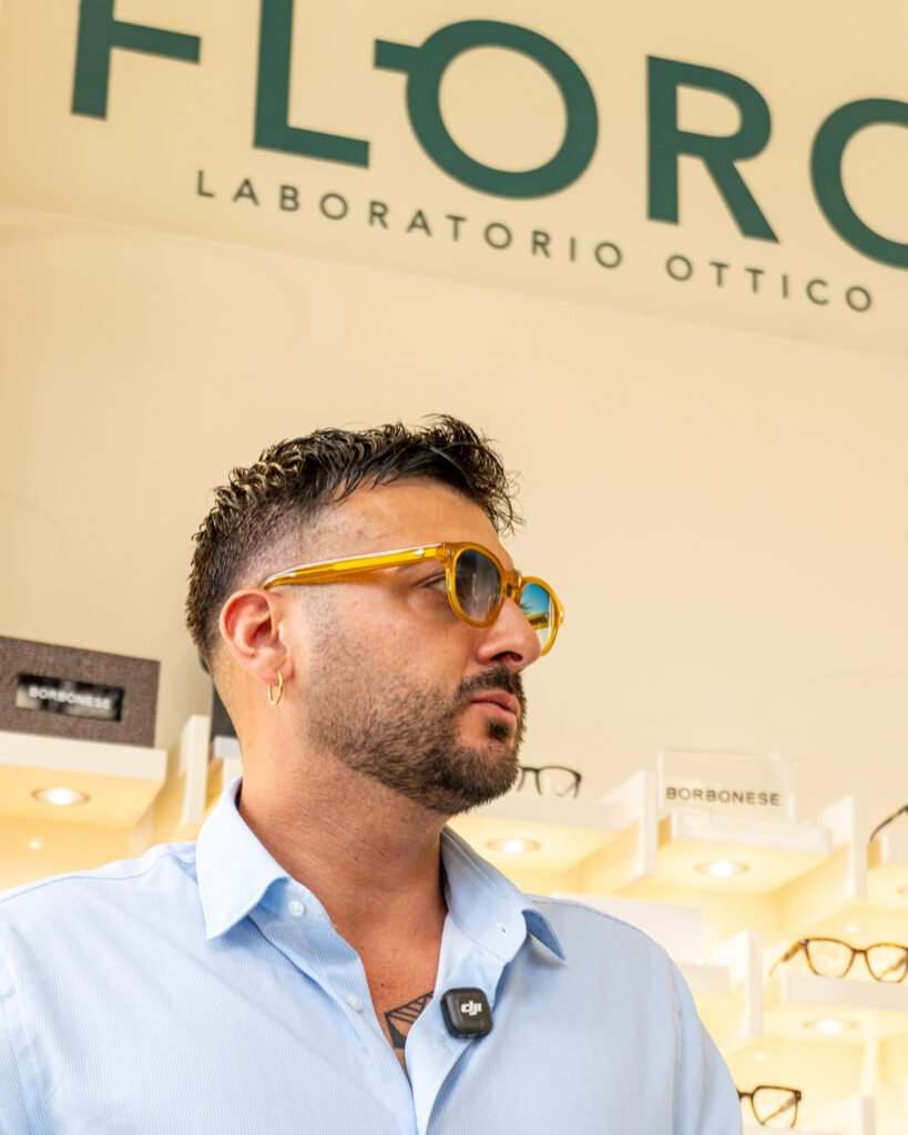 Uomo con occhiali da sole tondi in acetato miele sotto l'insegna Floro Laboratorio Ottico