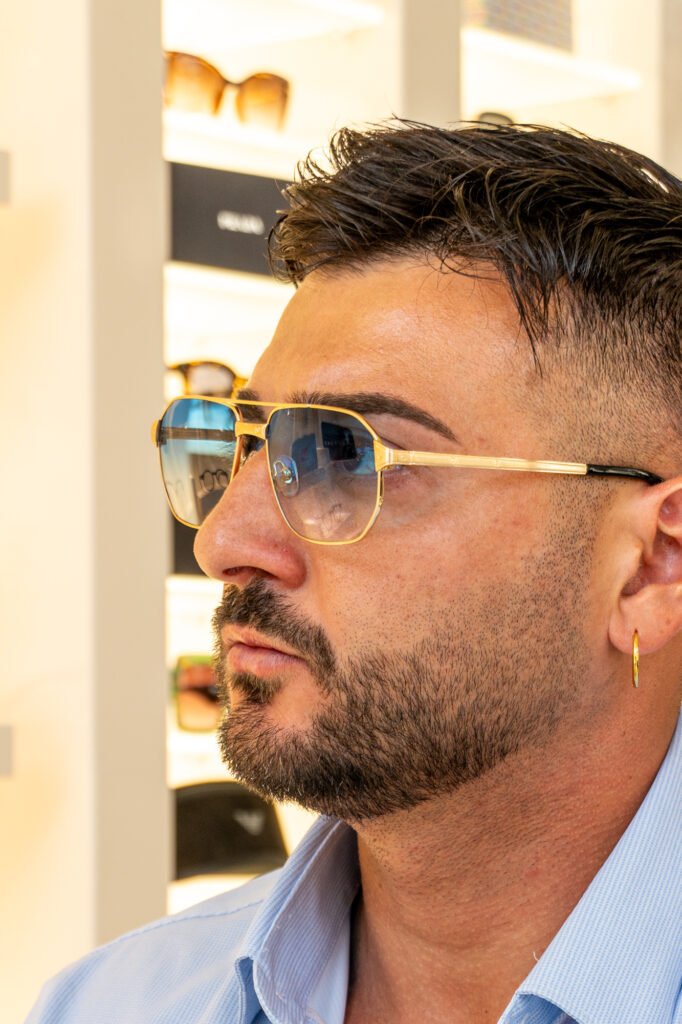Uomo indossa occhiali da sole aviator con montatura dorata e lenti sfumate azzurre